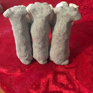 May include: Three gray clay sculptures of legs, standing upright on a red surface.