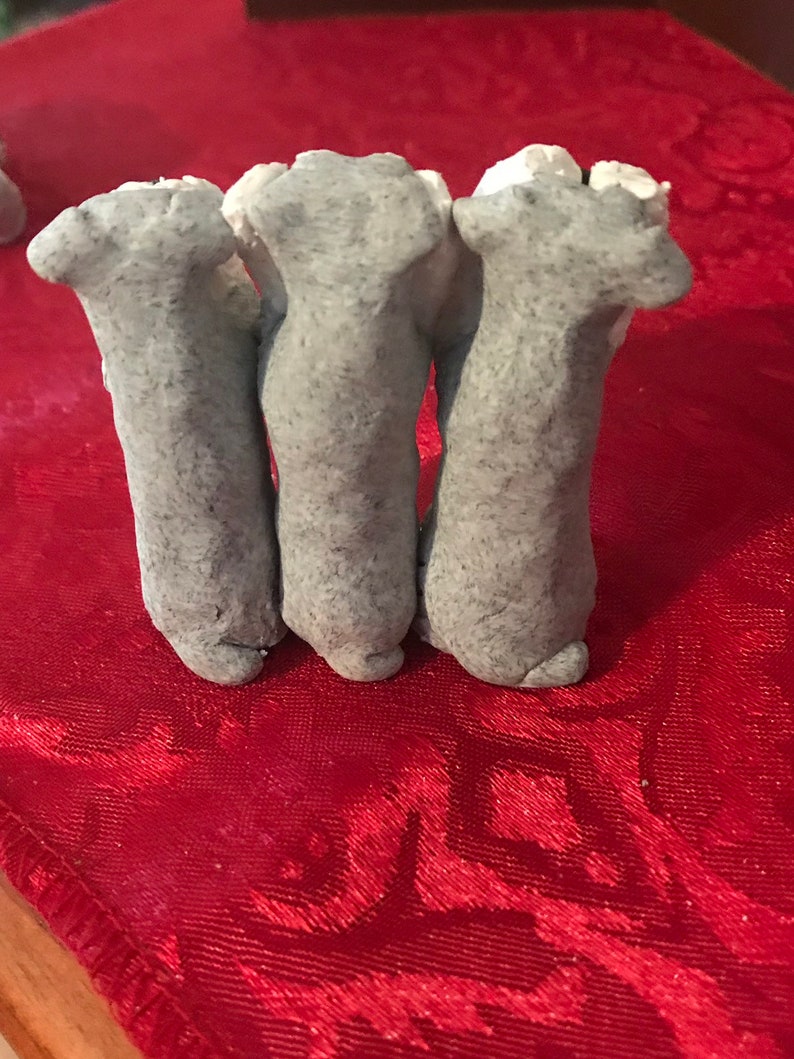 May include: Three gray clay sculptures of legs, standing upright on a red surface.