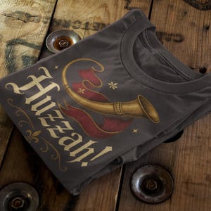 Vintage style Huzzah t-shirt with trumpet and banner medieval design folded on rustic wood.