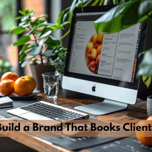May include: A desktop computer with a silver frame and black keyboard sits on a wooden desk. The screen displays a website with images of apples. The text "Build a Brand That Books Clients" is at the bottom of the image. Oranges, plants, and a glass of water are also on the desk.