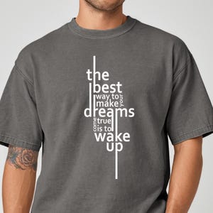 May include: A grey t-shirt featuring the white text: "the best way to make your dreams come true is to wake up." The shirt has a crew neck and short sleeves.