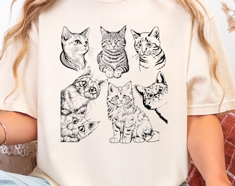 May include: Cream-colored t-shirt featuring a collection of black and white cat illustrations. The drawings depict various cat poses and expressions, showcasing different breeds and styles. The shirt is made of a soft material.