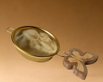 Colador de té artesanal de acero inoxidable con forma de mariposa dorada.
