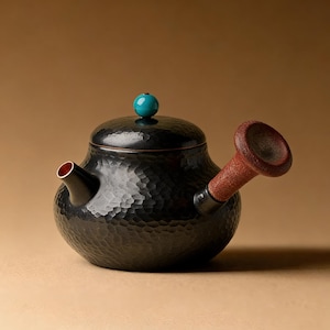 May include: A black hammered-texture teapot with a brown spout and a turquoise knob on the lid. The teapot has a small spout with a red interior. The handle is a dark brown color.