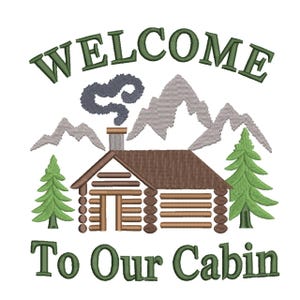 May include: Embroidered design featuring a log cabin with a smoking chimney, two green pine trees, and mountain range. The text "WELCOME" arches above the cabin, with "To Our Cabin" below, all in green thread.