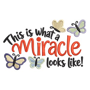May include: An embroidered design with the phrase "This is what a Miracle looks like!" in black and red. The design includes several embroidered butterflies in various colors, including purple, blue, and tan, on a white background.