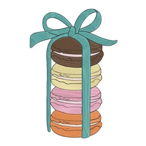 Peut inclure: Un motif brodé représentant une pile verticale de quatre macarons ronds de couleur marron, jaune, rose et orange, chacun avec une garniture à la crème visible. La pile est attachée par un ruban bleu sarcelle formant un grand nœud au sommet.