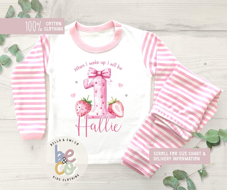 May include: A white and pink striped pajama set for a child. The top has pink sleeves and a pink collar. The front of the top features a large pink number 1 with strawberries and the name "Hallie". The text "When I wake up I will be" is above the number.