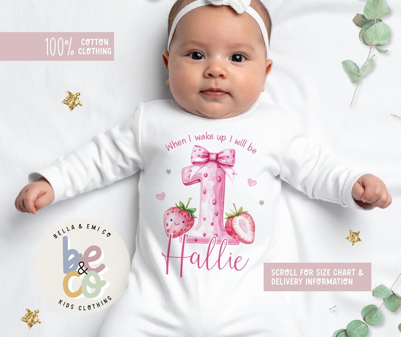 May include: White baby onesie with a pink number one design, strawberries, and the name "Hallie." The onesie has the text "When I wake up I will be." The words "100% Cotton Clothing" and "Bella & Emi Co Kids Clothing" are also visible.
