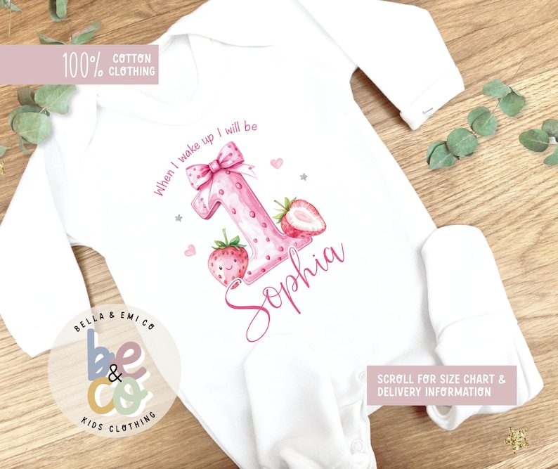 May include: White baby onesie with long sleeves. The onesie features a large pink number one with strawberry accents, the name "Sophia", and the text "When I wake up I will be". The onesie is made of 100% cotton.