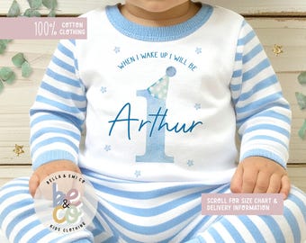 May include: A white and light blue striped cotton pajama set for a baby. The top features the text "WHEN I WAKE UP I WILL BE Arthur" with a number one and party hat graphic. The set is labeled "100% Cotton Clothing".