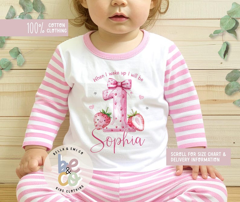 May include: White and pink striped pajama set for a child. The long-sleeved top features a large pink number "1" with a bow, strawberries, and the name "Sophia". The text "When I wake up I will be" is above the number. The set is made of 100% cotton.