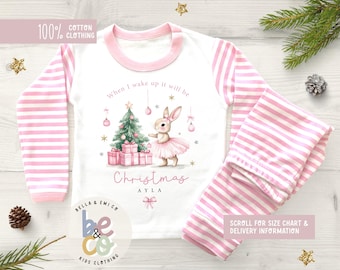 May include: White and pink striped Christmas pajamas set. The top has a pink trim and sleeves with pink stripes. The front features a Christmas tree, a bunny wearing a tutu, and the word "Christmas". The text "100% Cotton Clothing" is also visible.