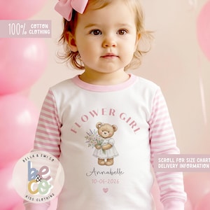 May include: A white and pink long-sleeved shirt with the text "FLOWER GIRL" and a teddy bear illustration. The shirt also features the name "Annabelle" and the date "10-06-2026". The shirt is made of 100% cotton clothing.