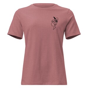 Könnte beinhalten: Staubrosa T-Shirt mit einer schwarzen Strichzeichnung eines Frauenprofils mit aufwendiger Hochsteckfrisur. Das kurzärmelige Shirt ist aus weichem Material und hat einen klassischen Rundhalsausschnitt.