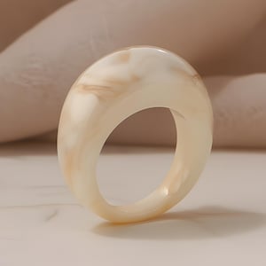 Op de afbeelding: Een crèmekleurige ring met een afgeronde, ovale vorm. De ring heeft een gemarmerd uiterlijk met lichtbruine en crèmetinten. De ring staat tegen een neutrale achtergrond.
