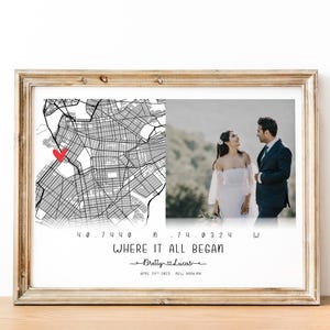 May include: Framed print with a map and a photo of a couple. The map has a red heart marking a location. Text reads "WHERE IT ALL BEGAN" with names and a date. The frame is a light brown color.