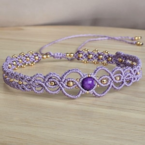 Può includere: Braccialetto in macramè lavanda fatto a mano con perline dorate e una gemma viola centrale. Il braccialetto presenta un'intricata lavorazione a nodi e lacci regolabili per una vestibilità confortevole.