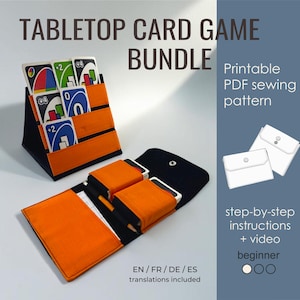 May include: A tabletop card game bundle featuring a black and orange fabric card holder with three tiers for cards, and a matching black and orange fabric folding wallet with pockets for cards and a pencil. Includes text: TABLETOP CARD GAME BUNDLE.
