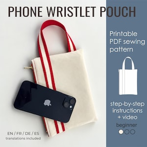 Op de afbeelding: Een naaipatroon voor een telefoonpolsbandje met een crèmekleurig stoffen tasje, rood-wit gestreepte hengsels en een gouden rits. Een zwarte smartphone ligt erbovenop. De tekst bevat PHONE WRISTLET POUCH, Printable PDF sewing pattern, step-by-step instructions + video, beginner en EN / FR / DE / ES translations included.