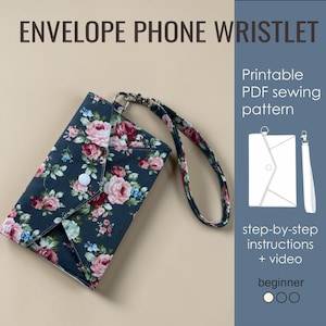 May include: An envelope phone wristlet with a floral pattern in pink, red, and blue on a dark background. The wristlet has a white button closure and a matching strap. The image also includes text that says "ENVELOPE PHONE WRISTLET".