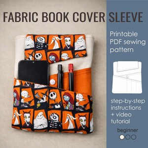 May include: Fabric book cover sleeve with a black smartphone, pens, and a button. The cover has an orange and black pattern with characters. The text on the image says "FABRIC BOOK COVER SLEEVE" and "Printable PDF sewing pattern".