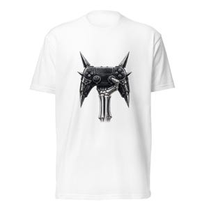 May include: White t-shirt featuring a detailed black and gray graphic of a video game controller with spikes and a skeletal hand. The controller design has buttons and joysticks, giving it a unique, edgy look. The shirt is made of a soft material.