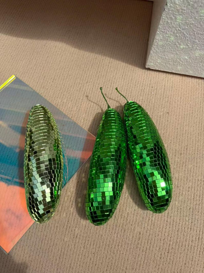 May include: Three green disco ball-style ornaments. Two are upright, and one is lying on its side. The ornaments are covered in small, reflective squares. The ornaments have a stem at the top.
