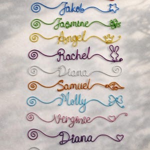 以下が含まれることがあります： カラフルなワイヤーネームアートのコレクション。各名前はユニークな色とスタイルで作成され、ハート、星、リボンなどの装飾的なアクセントが付いています。名前には、Leah、Jakob、Jasmine、Angel、Rachel、Diana、Samuel、Molly、Virginie、Diana、Lianeが含まれます。