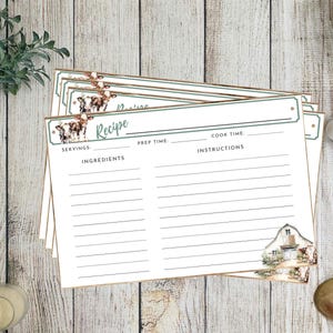 May include: A stack of recipe cards with a farmhouse theme. Each card has a green border and features a cow illustration. The cards are blank, with spaces for servings, ingredients, prep time, cook time, and instructions. The cards are on a wooden surface.