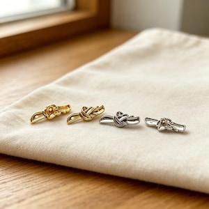 May include: Four toggle fasteners arranged in a row, featuring two gold-toned and two silver-toned pieces. Each fastener has a central knot design with extended ends, showing the front and back sides of the metal hardware components.