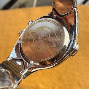 May include: A silver-toned Nike wristwatch, viewed from the back, showcasing the watch's stainless steel construction. The watch face features the Nike logo and the text "Stainless Steel Movement Japan Assembled in China H20 Resist 50M".