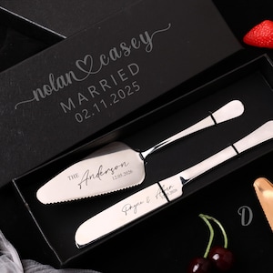 Può includere: Un set di paletta e coltello per torte argentati in una scatola nera. Il server è inciso con "The Anderson 12.05.2026". Il coperchio della scatola recita "nolan & casey MARRIED 02.11.2025". Fragole e ciliegie sullo sfondo.
