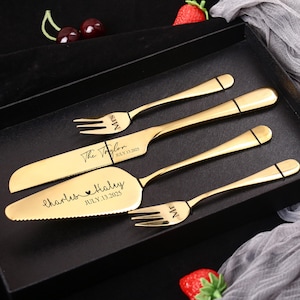 May include: A gold-colored wedding cake serving set with two forks and a cake knife and server, presented in a black box. The set is engraved with names and a date. The forks are marked "Mr" and "Mrs".