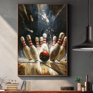 Puede incluir: Una obra de arte enmarcada representa una escena de bolos. La imagen muestra una bola de bolos roja golpeando bolos blancos con rayas rojas. El fondo es oscuro con salpicaduras blancas y rojas, lo que sugiere movimiento e impacto. La obra está enmarcada.