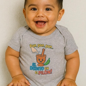 May include: A smiling baby wearing a gray onesie with the text "Pon, pon, pon... El Dedito en El Pilón!" and a cartoon mortar and pestle graphic. The onesie is short-sleeved and has a light gray color.
