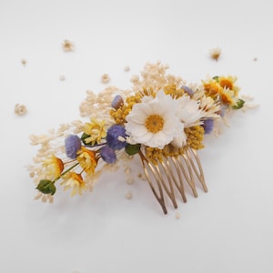 Könnte beinhalten: Ein Haarkamm mit getrockneten Blumen in Weiß, Gelb und Lila. Die Blumen sind auf einem goldfarbenen Kamm angeordnet. Dieser Kamm eignet sich für Hochzeiten oder besondere Anlässe und verleiht dem Haar einen natürlichen Look.