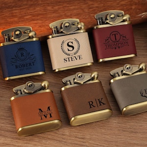 Puede incluir: Seis encendedores metálicos rectangulares con revestimientos de cuero sintético en azul, crema, granate, tostado, marrón y gris. Cada encendedor tiene un mecanismo superior de tono latón y grabados láser personalizados con monogramas.