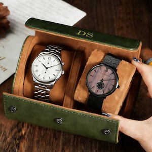 May include: A green leather watch case with two watches. One watch has a silver band and white face. The other watch has a black band and a wood-grain face. The case is embossed with the initials "DS".