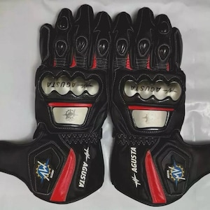 Peut inclure: Paire de gants de moto noirs avec des détails rouges et des plaques de protection argentées. Les gants affichent le logo "MV AGUSTA" en blanc et un emblème bleu et jaune. Conçus pour la protection et la performance.