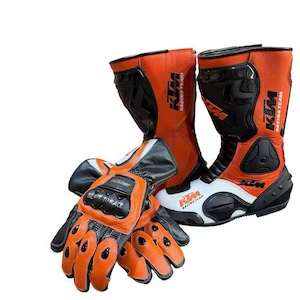 Könnte beinhalten: Orange und schwarze Motorradstiefel und -handschuhe. Die Stiefel haben weiße Akzente und das KTM Racing Team Logo. Die Handschuhe sind orange und schwarz mit dem Text "READY TO RACE".