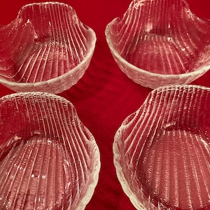 May include: A set of four clear glass bowls, each featuring a textured, ribbed exterior design that mimics the appearance of a seashell. The bowls have a rounded, scalloped rim and a deep, concave interior, providing a uniform look for the collection.