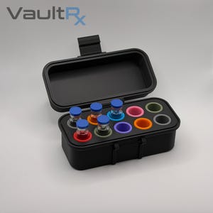 May include: Black carrying case with an open lid, holding several small glass vials with blue caps and colorful bases. The case has a handle and the text "VaultRx" is visible in the upper left corner.