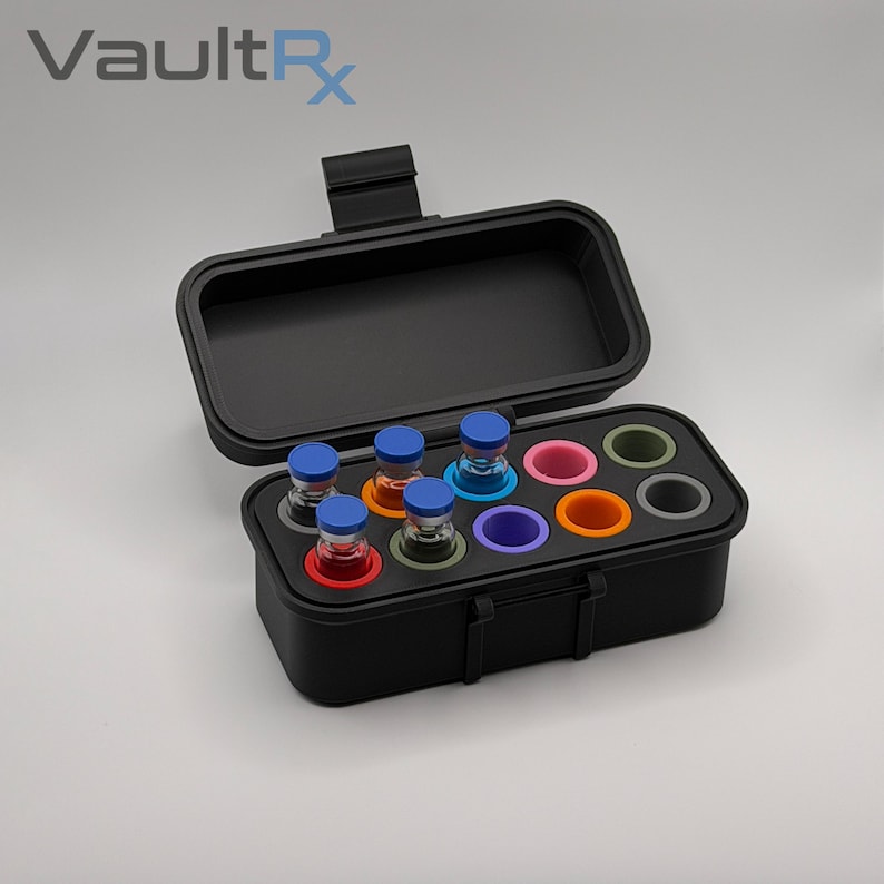 May include: Black carrying case with an open lid, holding several small glass vials with blue caps and colorful bases. The case has a handle and the text "VaultRx" is visible in the upper left corner.