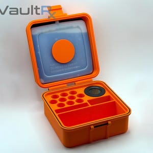 May include: An open orange storage container with a blue ice pack and an orange circle. The container has compartments for organization. The text "VaultRx" is in the upper left corner. The container is on a white background.