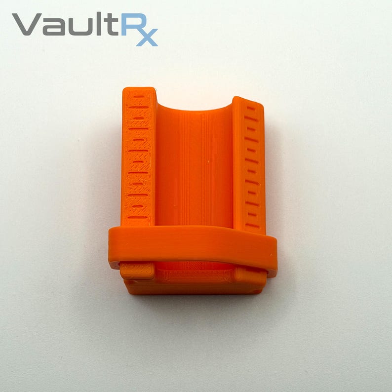 May include: Bright orange 3D-printed device with vertical measurement markings on both sides. The device has a curved interior and the text "VaultRx" is visible in the upper left corner.