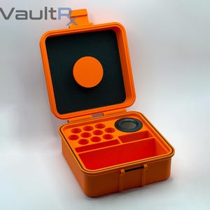 May include: Open orange storage case with black interior foam and a circular orange lid. The case has multiple compartments and a black circular insert. The case is designed to protect and organize small items.