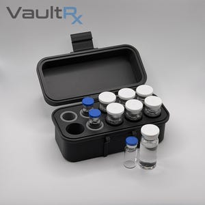 May include: Black storage case with a hinged lid, holding several small glass vials with white and blue caps. The case is open, revealing the vials inside. The text "VaultRx" is in the upper left corner.