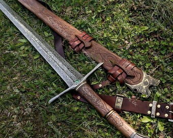 May include: A metal sword with an intricate etched blade, a green gemstone at the crossguard, and a brown wooden handle featuring carved patterns. It is accompanied by a matching brown leather scabbard with embossed designs and metal accents.