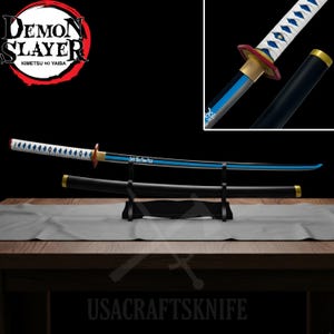 Könnte beinhalten: Ein Katana-Schwert mit schwarzer Scheide und Griff, ausgestellt auf einem schwarzen Ständer. Die Klinge ist blau und silber mit einem weißen Griff. Das Schwert hat einen roten und goldenen Knauf. Das Bild enthält den Text "DEMON SLAYER" und "USACRAFTSKNIFE".